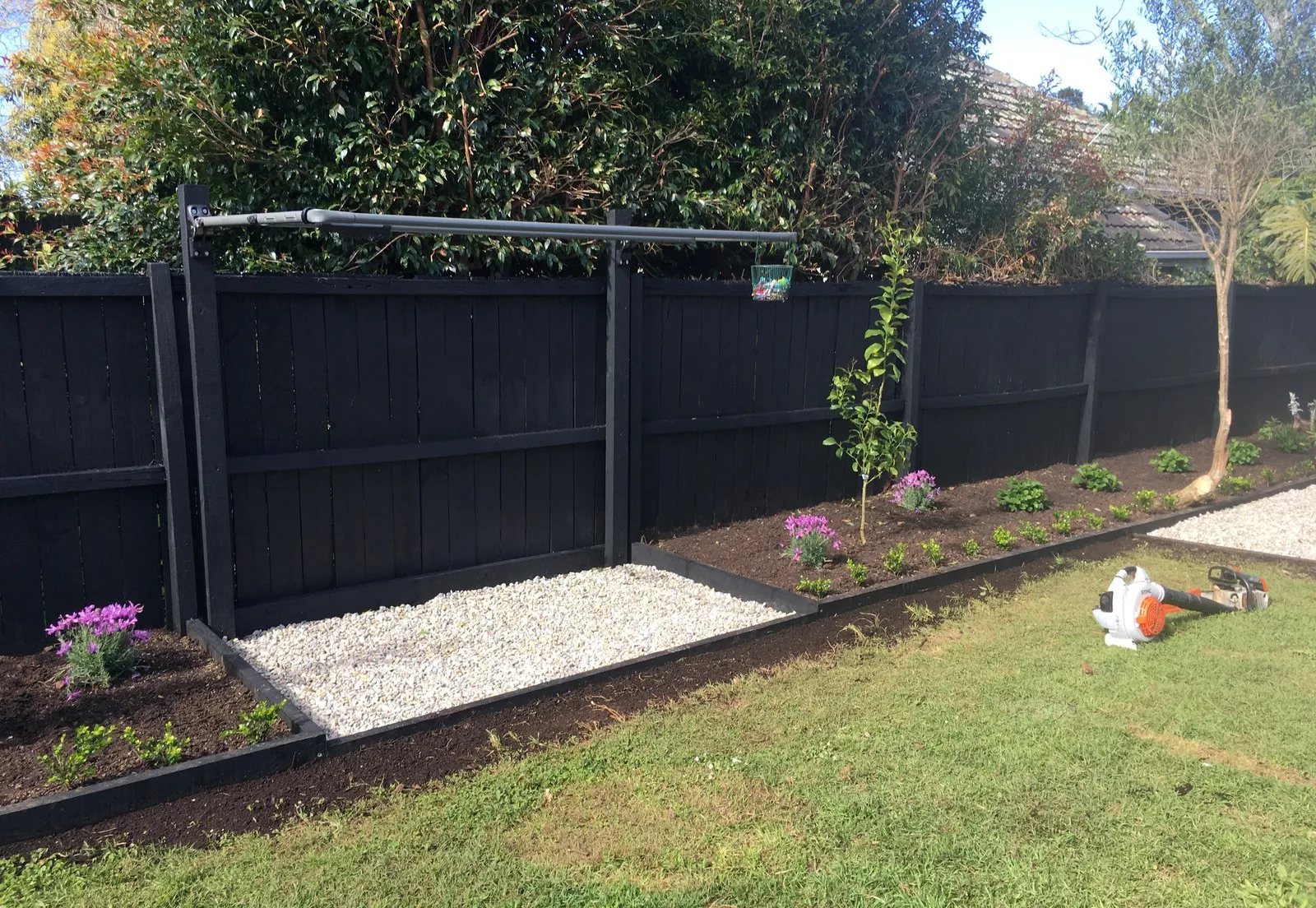 A dark stained fence above a new gravel path and fresh planting