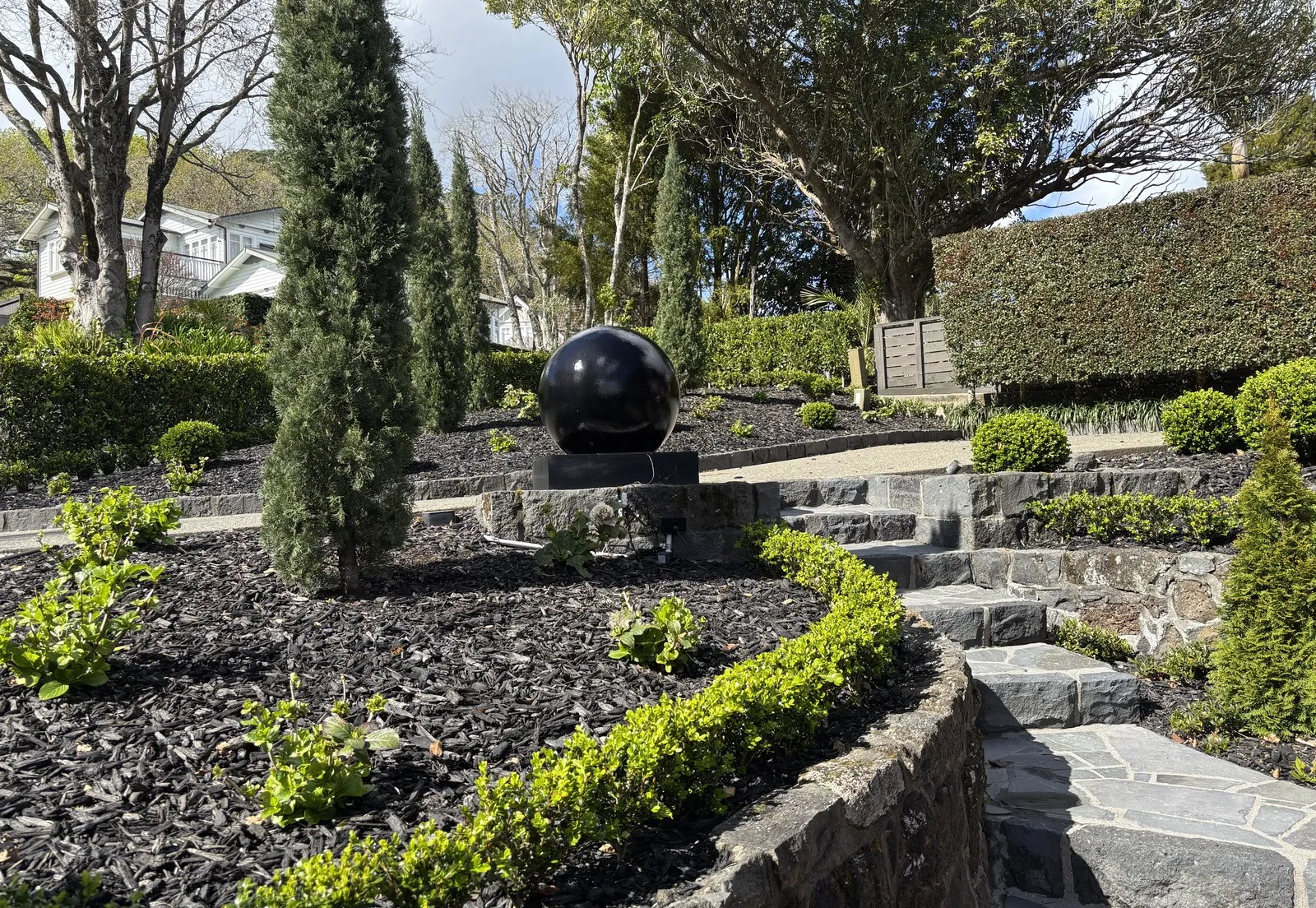 Terraced stone retaining walls with clipped box hedging and black mulch